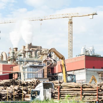 industrial plant of a furniture factory with smoking smokestacks,tubes,silos,crane ,truck and trunks.