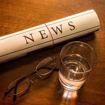 newspaper, glass water, glasses on desk