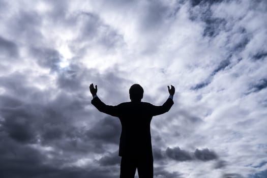 businessman upholding arms and stormy clouds