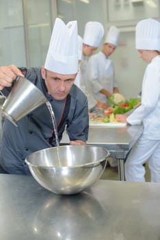 Chef pouring liquid into stainless steel bowl