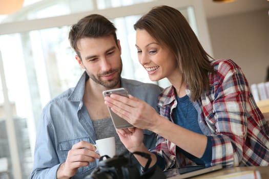 Couple in coffee shop looking at pictures on smartphone