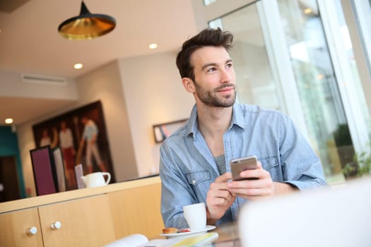 Man in coffee shop sending message with smartphone