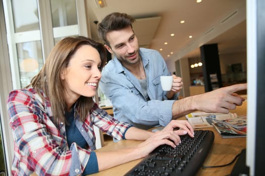 Couple in coffee shop websurfing on desktop computer