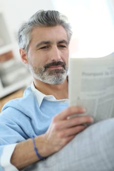 Mature man reading newspaper sitting in sofa