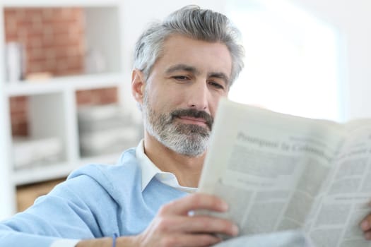 Mature man reading newspaper sitting in sofa