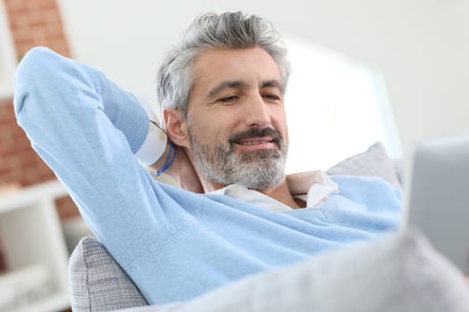 Mature handsome man websurfing on tablet at home
