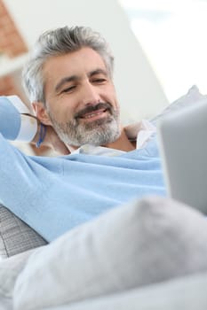 Mature handsome man websurfing on tablet at home