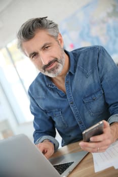 Teacher using laptop and smartphone in school office