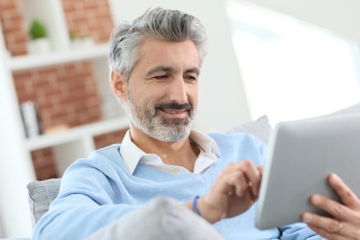 Mature handsome man websurfing on tablet at home