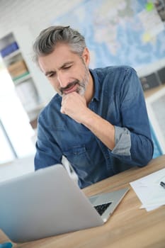 Mature man working on laptop in school office
