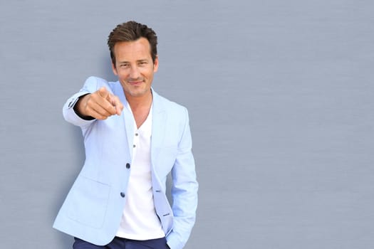 Mature man on grey background pointing at camera