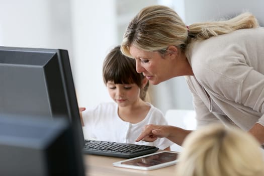 Teacher with little girl in class using computer and tablet