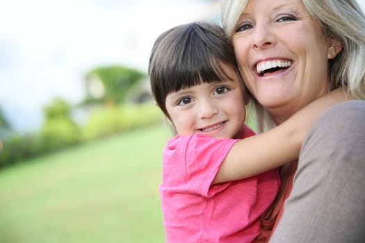 Cheerful woman embracing little girl in arms