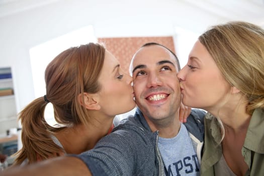 Cheerful guy taking picture of girls kissing him