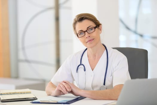 Portrait of mature nurse sitting at desk in office