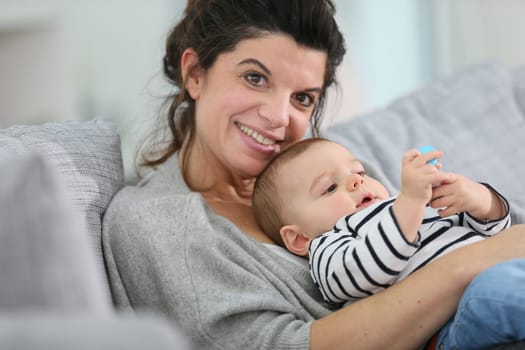 Cheerful mother cuddling in sofa with baby son