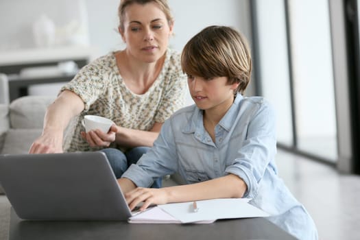 Mother looking after son doing homework on laptop