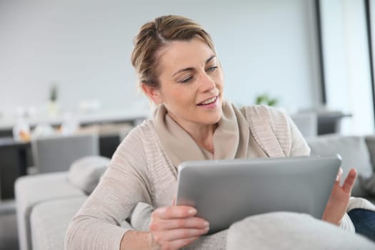 Mature woman sitting in sofa and websurfing with tablet