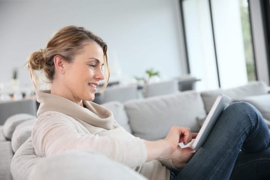 Mature woman sitting in sofa and websurfing with tablet