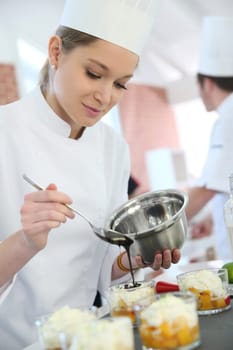 Pastry cook student pouring chocolate sauce on dessert