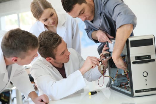 Students in computing class with teacher fixing hardware