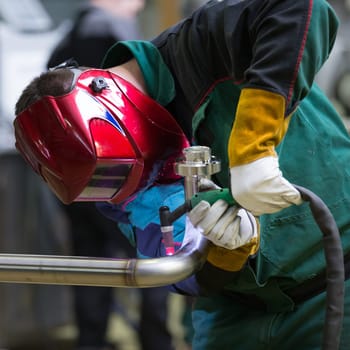 Industrial worker with protective mask welding inox elements in steel structures manufacture workshop.