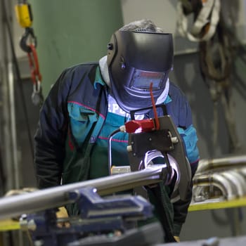 Industrial operator setting  computer controlled process of orbital welding machine in inox pipes manufacturing workshop.