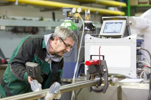 Industrial operator setting  computer controlled process of orbital welding machine in  stainless steel pipes manufacturing workshop.