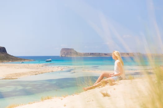 Relaxed woman enjoying sun, freedom and life an a beautiful sandy beach of Balos in Greece. Young lady feeling free, relaxed and happy. Vacations, freedom, happiness, enjoyment and well being.