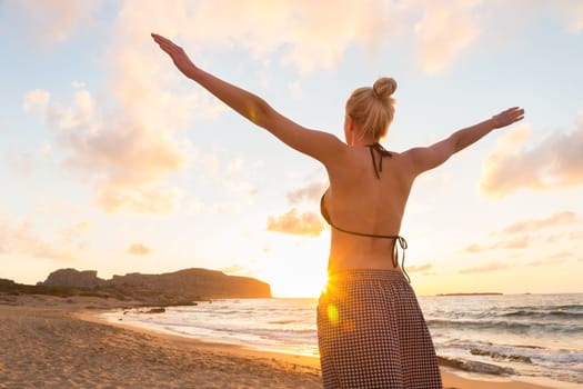 Relaxed woman, arms rised, enjoying sun, freedom and life an beautiful beach in sunset. Young lady feeling free, relaxed and happy. Concept of vacations, freedom, happiness, enjoyment and well being.