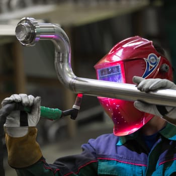 Industrial worker with protective mask welding inox elements in steel structures manufacture workshop.
