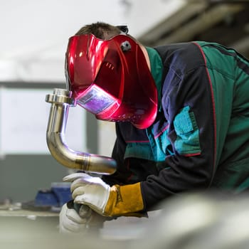 Industrial worker with protective mask welding inox elements in steel structures manufacture workshop.