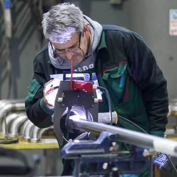 Industrial operator setting  computer controlled process of orbital welding machine in  stainless steel pipes manufacturing workshop.
