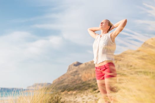 Relaxed woman, arms rised, enjoying sun, freedom and life an a beautiful beach. Young lady feeling free, relaxed and happy. Concept of vacations, freedom, happiness, enjoyment and well being.