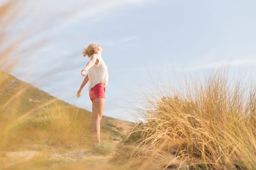 Relaxed woman, arms rised, enjoying sun, freedom and life an a beautiful beach. Young lady feeling free, relaxed and happy. Concept of vacations, freedom, happiness, enjoyment and well being.
