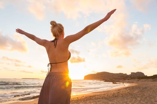 Relaxed woman, arms rised, enjoying sun, freedom and life an beautiful beach in sunset. Young lady feeling free, relaxed and happy. Concept of vacations, freedom, happiness, enjoyment and well being.