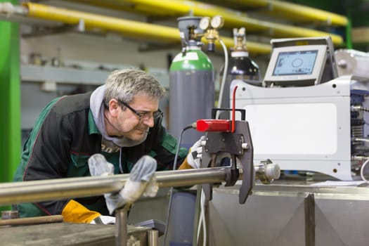 Industrial operator setting  computer controlled process of orbital welding machine in  stainless steel pipes manufacturing workshop.