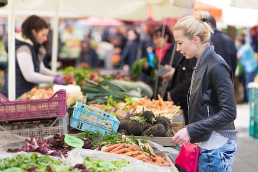 Woman buying fruits and vegetables at local food market. Market stall with variety of organic vegetable.