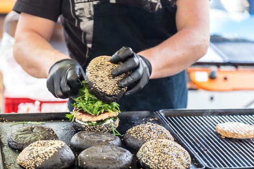 Chef making beef burgers outdoor on open kitchen international food festival event. Street food ready to serve on a food stall.