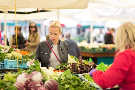 Woman buying fruits and vegetables at local food market. Market stall with variety of organic vegetable.