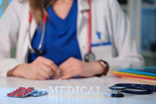 A medical professional writes a prescription surrounded by medications and essential healthcare tools