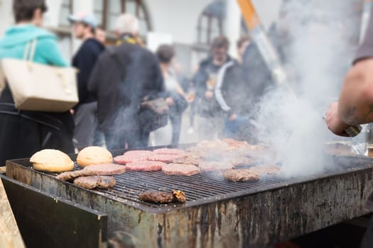 Chef making beef burgers outdoor on open kitchen international food festival event. Street food ready to serve on a food stall.