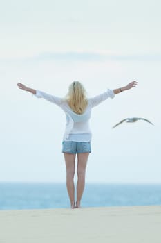 Woman enjoying freedom feeling as a bird at beach at dusk. Serene relaxing woman in pure happiness and elated enjoyment with arms raised outstretched up.