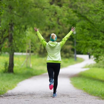 I have made it. Sporty young female runner arms rised in city park.  Running woman during outdoor workout in nature. Fitness model outdoors. Weight Loss. Healthy lifestyle.