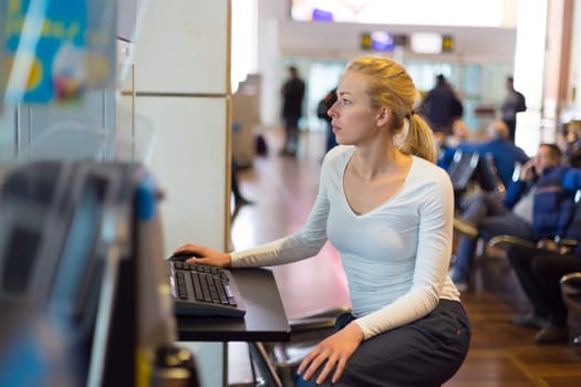 Young caucasian woman using comupter with public internet access point on airport.