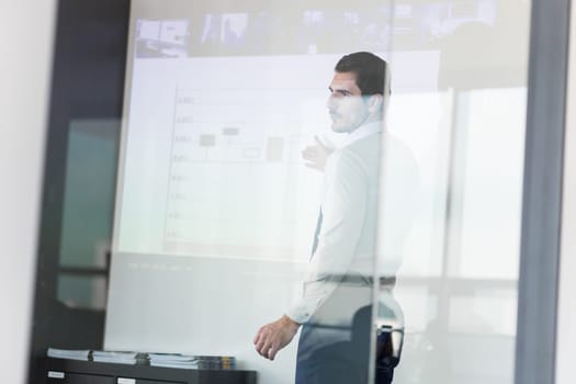 Business man making a presentation in front of whiteboard. View through glass.