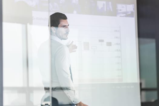 Business man making a presentation in front of whiteboard. View through glass.