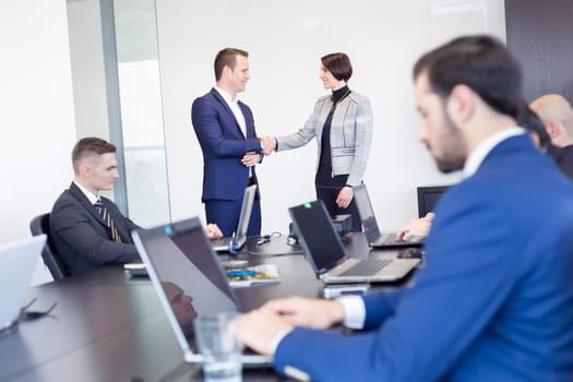Sealing a deal. Business people shaking hands, finishing up meeting in corporate office. Businessman working on laptop in foreground. Business and entrepreneurship concept.