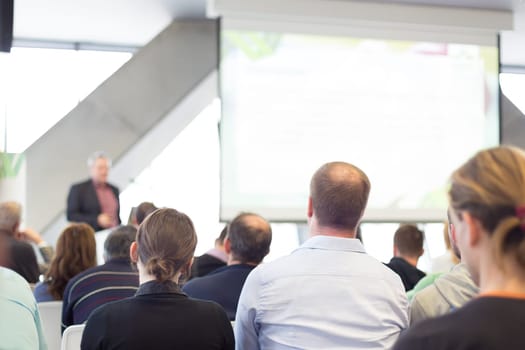 Man giving presentation in lecture hall. Male speeker having talk at public event. Participants listening to lecture. Rear view, focus on people in audience.