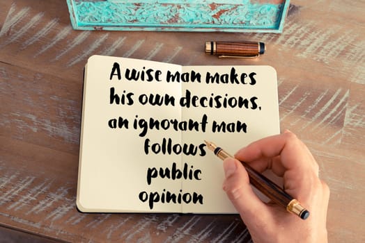 Retro effect and toned image of a woman hand writing on a notebook. Handwritten quote A wise man makes his own decisions, an ignorant man follows public opinion as inspirational concept image